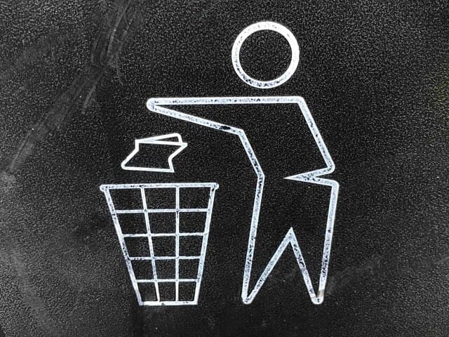 dibujo a tiza en pizarra negra mostrando silueta de persona arrojando papel a una papelera