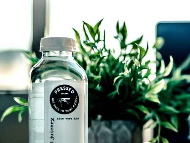 botella de agua de plástico transparente y planta verde de fondo